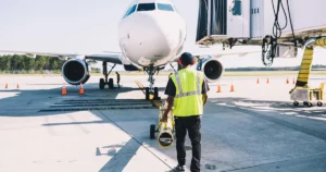 Personal de operaciones aeroportuarias trabajando en rampa junto a un avión comercial